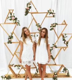 two girls standing next to each other in front of a backdrop with flowers and greenery