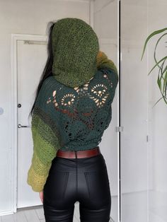 a woman wearing black leather pants and a green knitted hoodie standing in front of a mirror