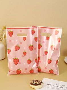 two pink bags with strawberries on them are sitting on a table next to a cookie