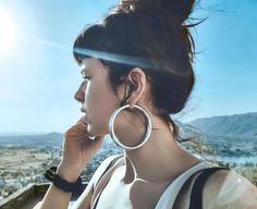 a woman with large hoop earrings on her ear looks out over the city skyline from atop a hill