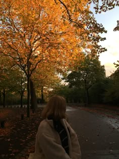 a woman is walking down the street in front of trees with orange leaves on it