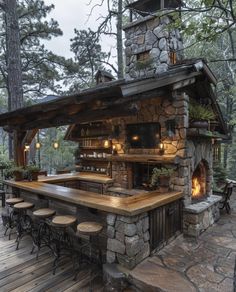 an outdoor bar with stools and tables in front of the fire place, surrounded by trees