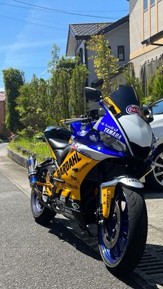 a blue and yellow motorcycle parked on the side of the road next to a car