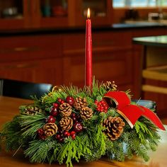 a christmas centerpiece with pine cones, berries and evergreens on a dining room table