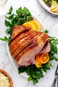 a large piece of meat sitting on top of a white plate next to sliced oranges and asparagus