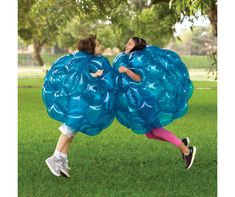 two girls are playing in the grass with giant balloons that look like they're hugging each other