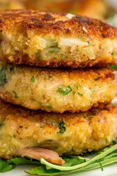 three crab cakes stacked on top of each other with greens and seasoning in the middle