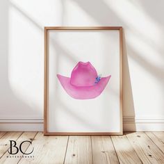 a pink cowboy hat is displayed in a wooden frame on the floor next to a white wall