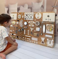 a young boy sitting on the floor next to a wooden board with various items and numbers