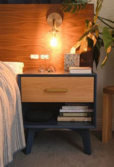 a night stand with books and a lamp next to it on top of a bed