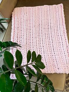 a pink crocheted blanket sitting on top of a table next to a plant