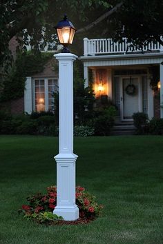 a white lamp post in front of a house with flowers on the ground and grass around it