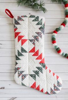 a christmas stocking with red, green and white decorations on it next to a pine tree