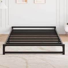 a black metal bed frame in a white room with two pictures on the wall behind it