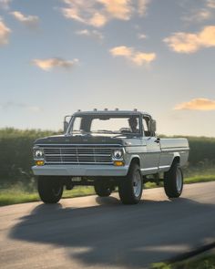 an old pick up truck driving down the road in front of some grass and trees