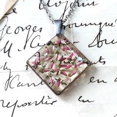 a square glass pendant with pink and white flowers in it on top of a piece of paper