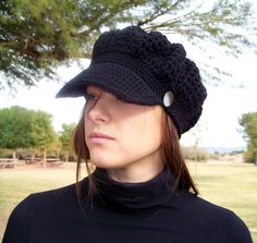 a woman wearing a black hat with a button on the side and a tree in the background