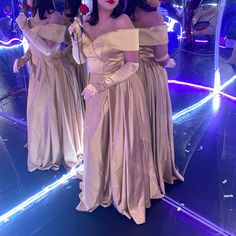 three women dressed in long dresses standing next to each other on a mirror floor with lights behind them