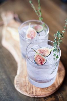 two glasses filled with water and sliced figs on top of a wooden board,