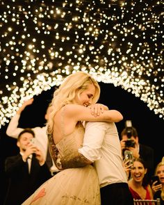 a man and woman hugging in front of a crowd with lights on the ceiling behind them