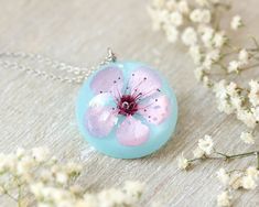 This cherry flower necklace is made from a real cherry flower picked up from the place where I live. A unique sakura necklace as the most unique birthday gift idea for women. In general, a cherry flower necklace (japanese flower necklace) is an outstanding full of significance complement for you. This sakura blossom necklace is part of my pale pink jewelry. The hypoallergenic stainless steel and the high-gloss crystalline resin gives this cherry flower necklace a precious and enamelled look. Use Delicate Pink Pendant Flower Necklace, Delicate Pink Flower Pendant Necklace, Handmade Pink Flower-shaped Necklace, Delicate Pink Flower Necklace For Gift, Spring Flower Pendant Jewelry Gift, Delicate Spring Necklaces For Gifts, Delicate Pink Necklace For Gift, Spring Flower-shaped Jewelry Gift, Spring Flower Charm Necklace For Gift