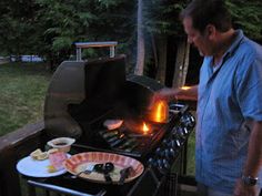 a man standing next to an outdoor grill with food on it and lit candles in front of him