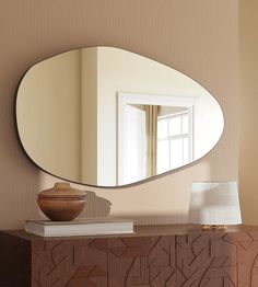 a mirror sitting on top of a wooden dresser next to a lamp and table with a vase