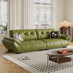 a green leather couch sitting on top of a white rug in a living room next to a window