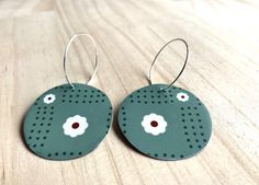 pair of green earrings with white and red flowers on wooden surface, closeup view