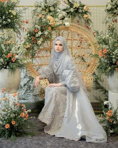 a woman wearing a hijab sitting on a chair in front of some flowers