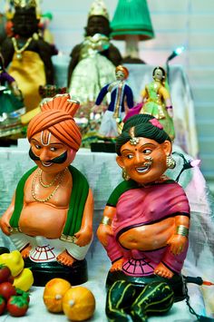 two figurines sitting on top of a table covered in fruit