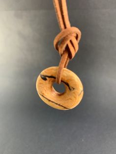 a small wooden object hanging from a rope on a gray surface with an orange cord