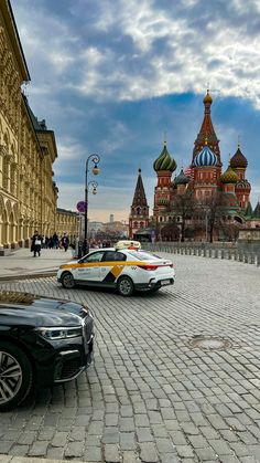 two cars parked in front of a building with domes on it's sides and people walking around