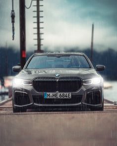 the front end of a silver bmw car parked on a dock in the rain with power lines above it