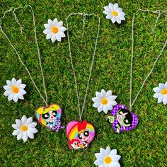 four necklaces with different designs on them laying in the grass next to daisies