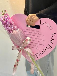 a person holding a pink heart shaped sign with flowers