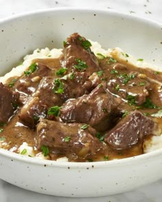 a white bowl filled with meat and gravy on top of mashed potatoes