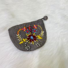 a small gray purse with colorful embroidered flowers on the front and sides, sitting on a white fur surface