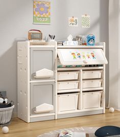 a child's play kitchen with white drawers and toys on the floor in front of it