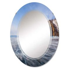 a round mirror sitting on top of a white wall next to a body of water