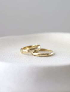 two gold wedding rings sitting on top of a white cake plate, with one ring in the shape of an arrow