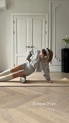 a woman in grey shirt and white pants doing push ups on wooden floor next to door