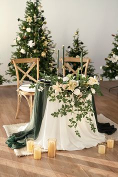 a table with candles and flowers on it in front of some christmas tree branches, surrounded by greenery