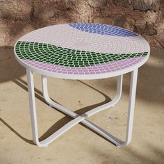 a white table with multicolored tiles on it sitting in front of a stone wall