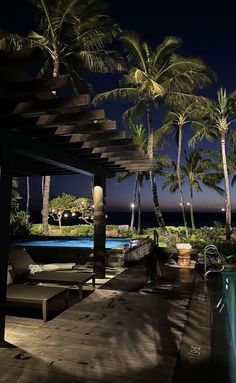 an outdoor swimming pool with lounge chairs and palm trees in the background at night time