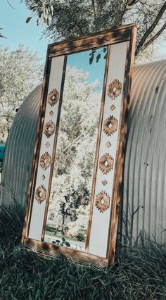 a large mirror sitting in the grass next to a metal structure with trees behind it