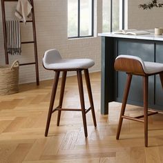 two stools in front of a kitchen island with white counter tops and wood floors