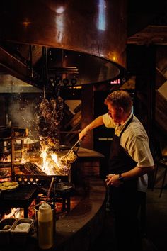 a man cooking food in a kitchen with flames coming out of the grills and on the counter