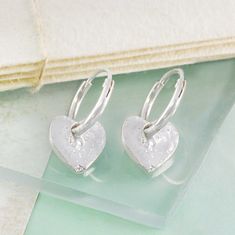 An incredibly simple and beautiful pair of solid silver earrings. These Organic Silver Heart Hoop Earrings are composed of a pair of dainty organically textured hearts suspended from elegant silver hoops. These Organic Silver Heart Hoop Earrings are available with a choice between a sleeper hoop or stud hoop with post and butterfly. If you would like this design in a gold or rose gold finish, please call us and we will offer this bespoke service. Made from: Sterling silver. Measurements: Hoops diameter: approx. 1.8cm. Heart Width: approx. 1cm. Earrings length: approx. 2.5cm. Silver Sterling Heart Charm Huggie Earrings, Silver Sterling Huggie Earrings With Heart Charm, Silver Huggie Earrings With Heart Charm For Anniversary, Silver Small Hoop Earrings With Heart Charm, Silver Hoop Earrings With Heart Charm For Anniversary, Heart-shaped Sterling Silver Huggie Earrings For Anniversary, Small Hoop Sterling Silver Heart Earrings Hypoallergenic, Hypoallergenic Small Hoop Heart Earrings In Sterling Silver, Nickel-free Double Heart Sterling Silver Hoop Earrings