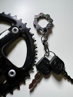 two keys attached to a bicycle chainring on top of a white table next to a black bike wheel